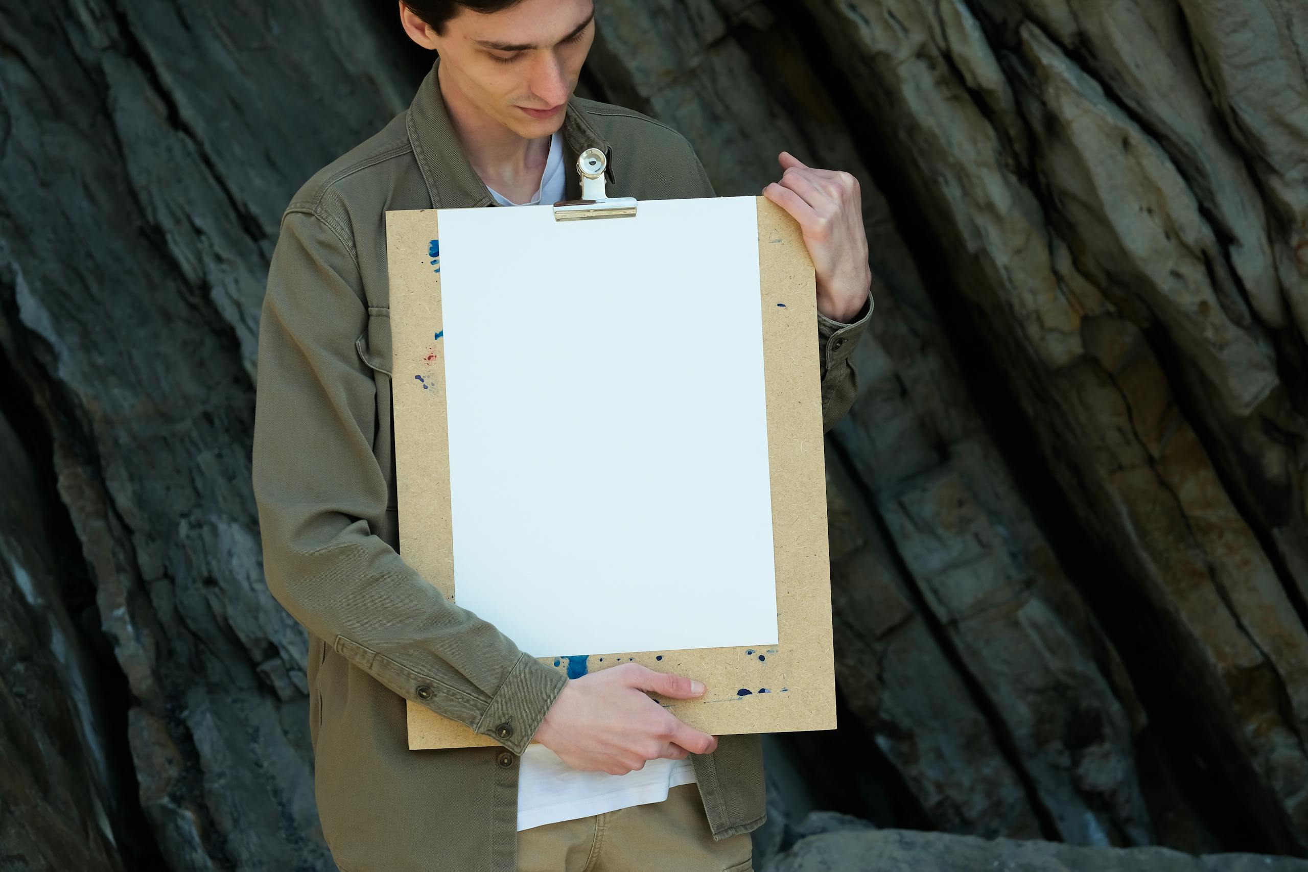 Adult holding an empty clipboard outdoors against a textured rock background.