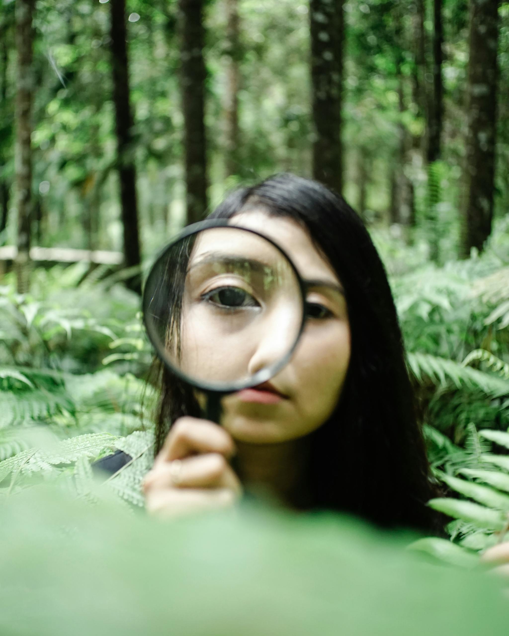Woman examining flora in a verdant forest with a magnifying glass, emphasizing discovery.